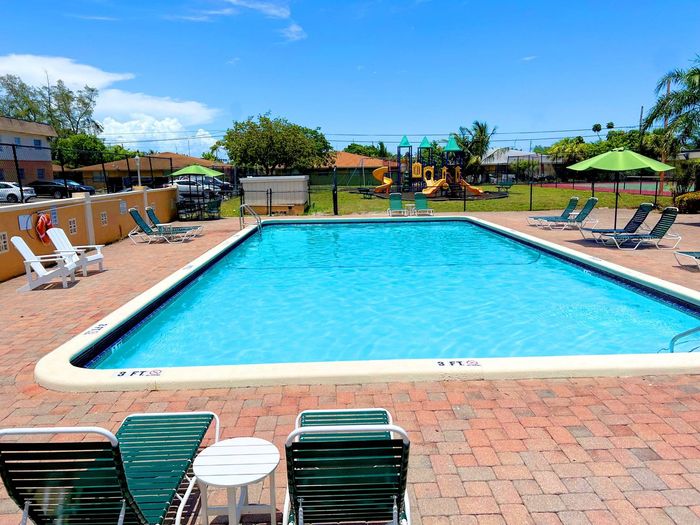 Pompano Palms Apartments, exterior, sparkling blue pool, picnic table with umbrella