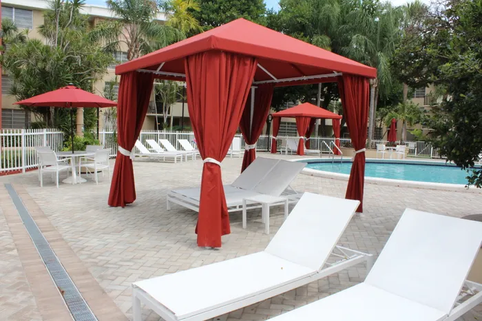 Colony at Dadeland Exterior | Outdoor pool | Pool chairs surrounding the pool | Red canopies over some chairs