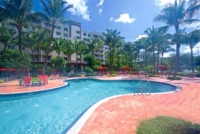 Royal Palms Apartments, exterior, sparkling blue pool, palm trees, lounge chairs, picnic tables with umbrellas, building exterior