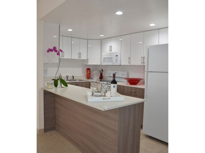 Pompano Palms Apartments, interior, kitchen, quartz counter tops, breakfast bar, white appliances stove, oven, refrigerator, tile flooring, white and brown cabinets
