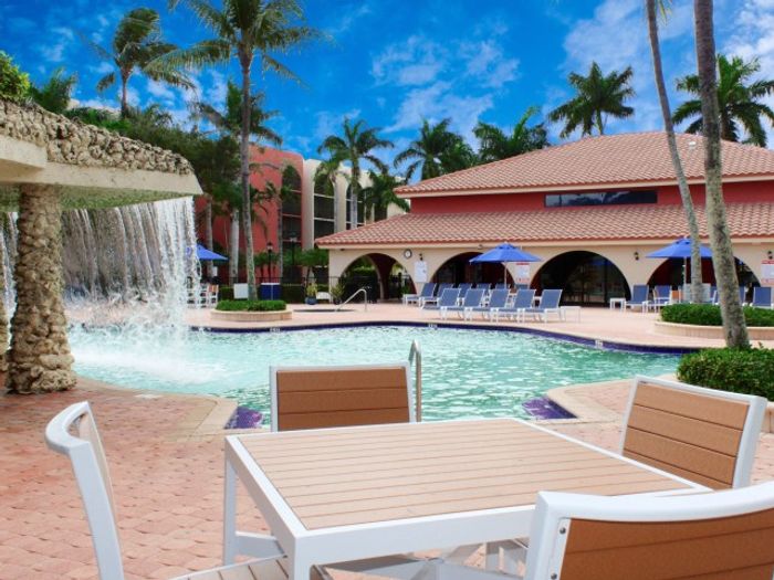 Aventura Harbor Apartments, exterior, palm trees, building exterior, sparkling blue pool, water fall, hot tub, lounge chairs, umbrella covered picnic tables. palm trees
