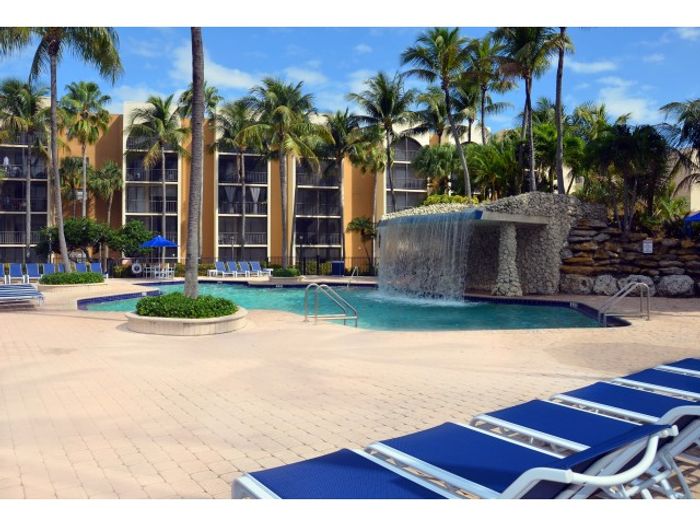 Aventura Harbor Apartments, exterior, sparkling blue pool, water fall, palm trees, umbrella covered picnic tables