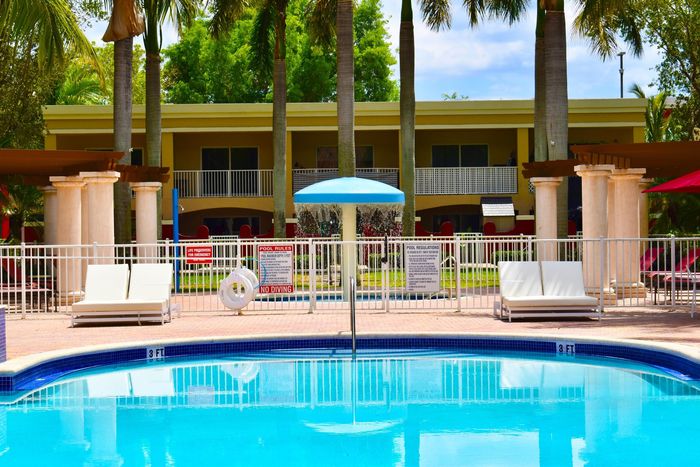 Country Club Towers, exterior, sparkling blue pool, blue lounge chairs, picnic table with umbrella, palm trees