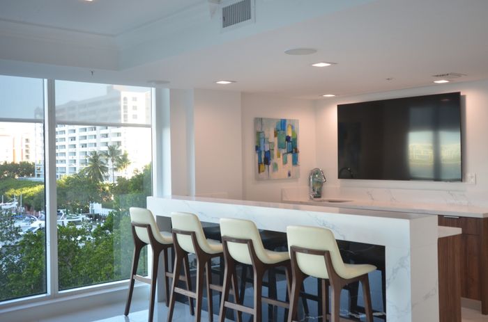 Bright kitchen area with a white marble countertop, bar seating, and a view of the cityscape through large windows.