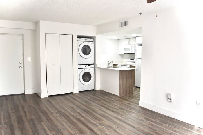 Chic apartment space featuring dark wood flooring, modern in-unit laundry, and a sleek kitchen area.