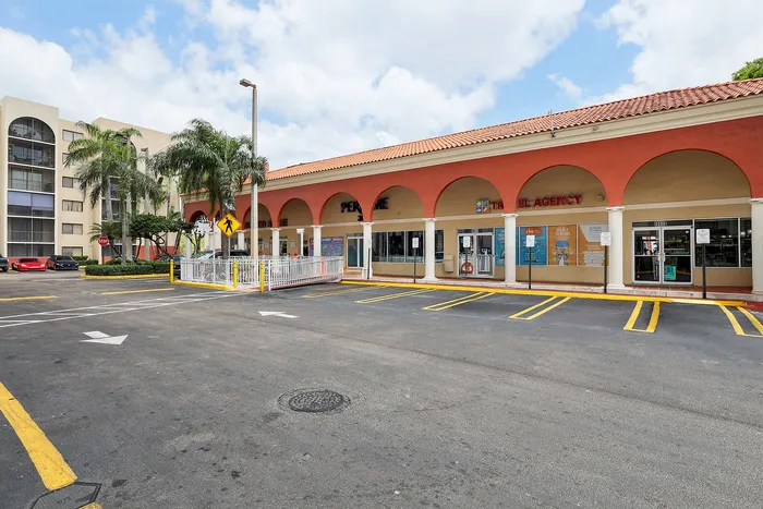 Charming retail plaza with red-tiled roof and arched walkways, featuring convenient parking space and lush palm trees.