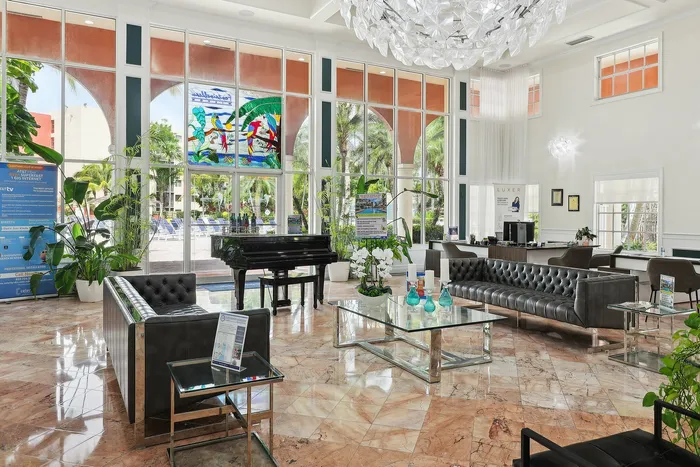 Luxurious apartment lobby featuring elegant marble floors, modern leather seating, a grand piano, and floor-to-ceiling windows with vibrant stained glass and lush garden views.