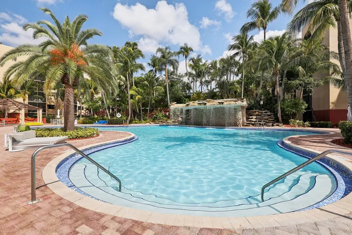 Luxurious resort-style swimming pool surrounded by lush palm trees and elegant waterfall feature, offering a tropical oasis for relaxation.