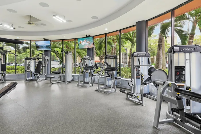 Modern fitness center with state-of-the-art gym equipment, surrounded by lush green palm trees, offering a refreshing workout space.