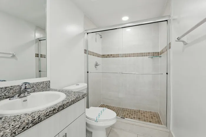Modern bathroom featuring a sleek glass-enclosed shower, granite countertop vanity, and elegant tile accents.