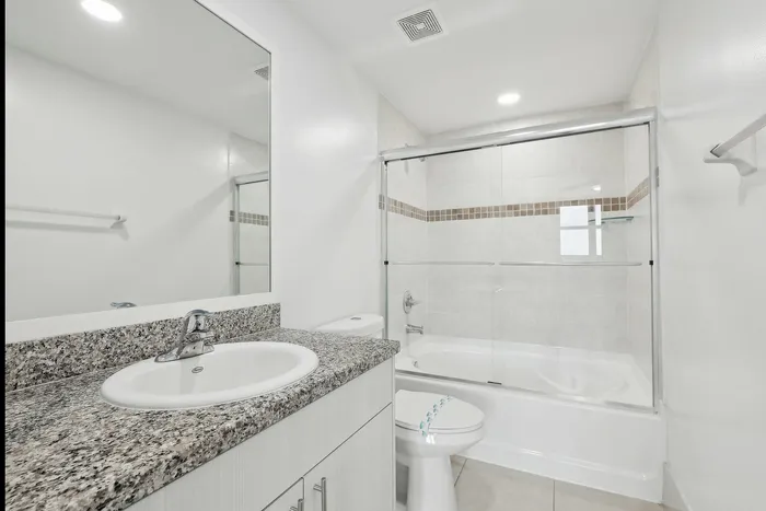 Modern, bright bathroom with elegant granite countertops, sleek fixtures, and a pristine glass-enclosed bathtub offering a contemporary feel.