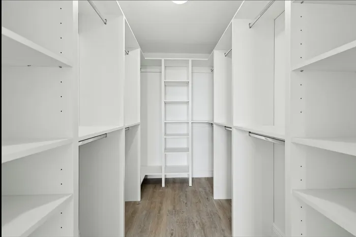 Spacious walk-in closet with sleek white shelving and ample hanging space, featuring elegant wood flooring.
