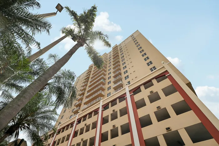 Impressive high-rise apartment building with modern architecture, surrounded by lush palm trees under a clear blue sky.