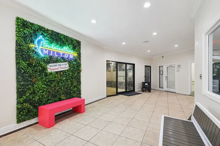Charming apartment entrance featuring a neon sign on a lush green wall, welcoming visitors to a tropical paradise with a vibrant red bench and stylish tile flooring.