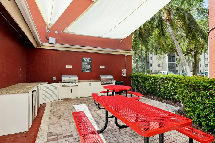 Inviting outdoor barbecue area with vibrant red picnic tables under a sunshade, perfect for entertaining.