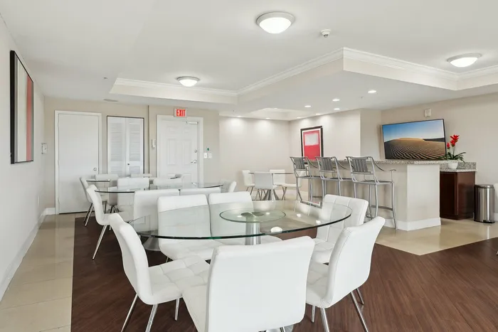 Modern communal lounge featuring elegant glass tables, plush white chairs, and a chic bar area with contemporary design.