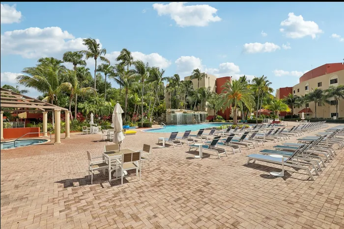 Luxurious outdoor swimming pool area with palm trees and sun loungers, offering a tropical paradise atmosphere.