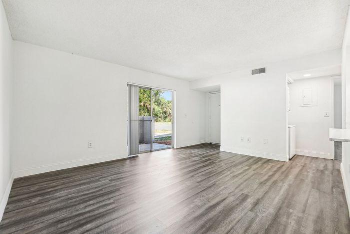 Bright and spacious living room with sleek wood flooring and large sliding glass doors leading to a serene outdoor space.