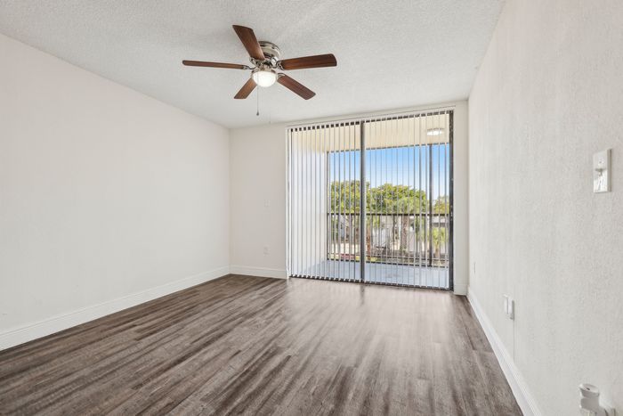 Bright and airy room with sleek hardwood floors, ceiling fan, and large sliding glass door leading to a scenic balcony view.