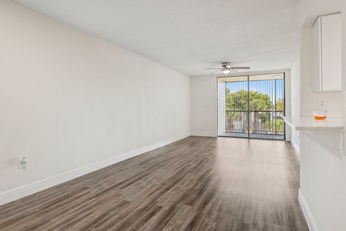 Bright living room with wood flooring and large sliding glass doors leading to a balcony, offering abundant natural light.