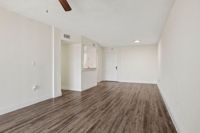 Spacious living area with elegant wood flooring, modern ceiling fan, and bright open layout.