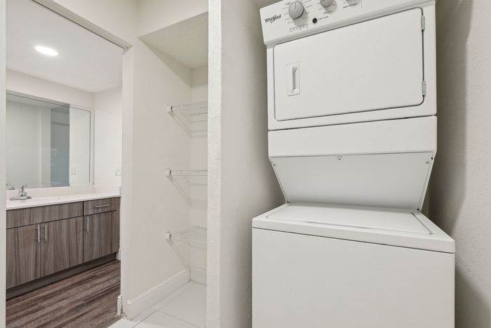 Modern apartment laundry area with stackable washer and dryer, adjacent to a sleek bathroom featuring elegant wood cabinetry and large mirrors.