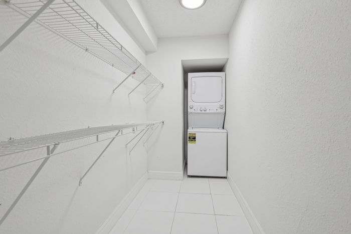 Bright laundry room featuring a convenient stackable washer and dryer, with ample shelving for storage.