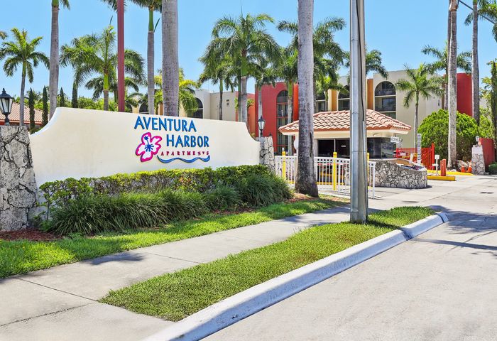 Charming entrance view of Aventura Harbor Apartments surrounded by tropical palm trees and lush landscaping.
