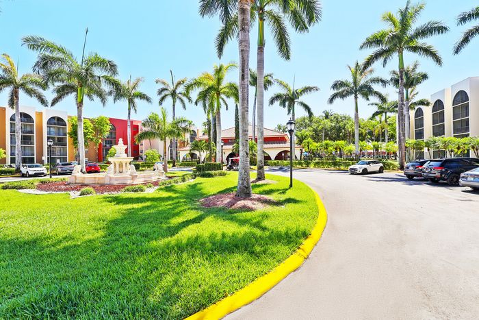 Luxurious apartment complex surrounded by lush palm trees and a serene fountain, showcasing modern architecture and vibrant landscaping.