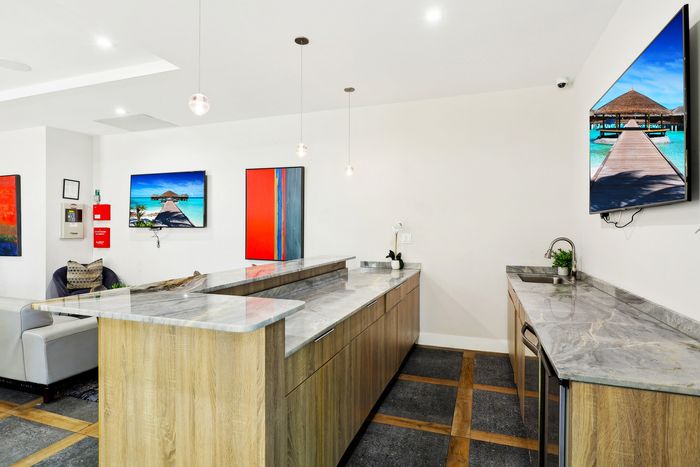 Contemporary kitchen interior featuring elegant marble countertops, modern wood cabinetry, and vibrant artwork on pristine white walls.