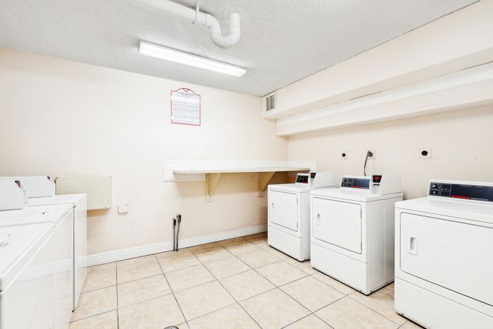 Bright and clean laundry room featuring multiple modern washers and dryers, ideal for convenient living.