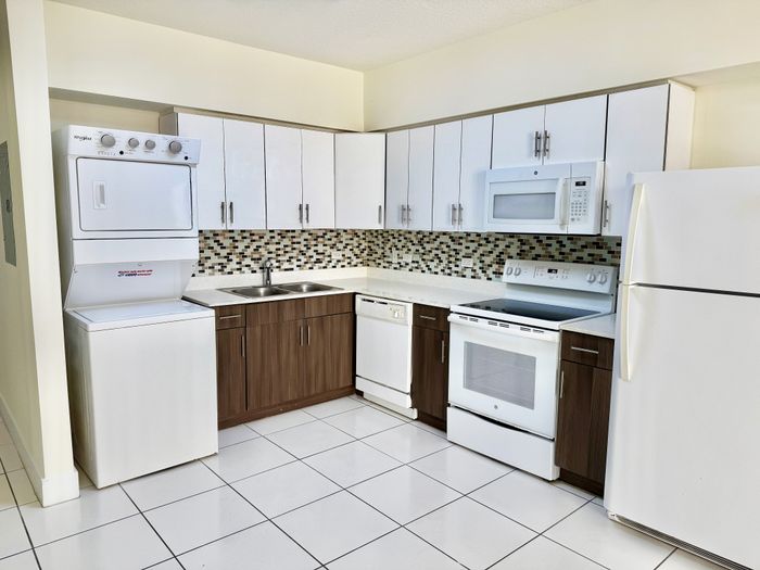 Modern kitchen with sleek white cabinets, stainless steel appliances, and stylish tile backsplash, featuring a convenient in-unit washer and dryer.