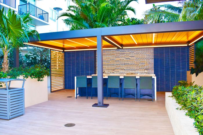 Chic outdoor seating area with modern pergola, vibrant greenery, and sleek blue accents.
