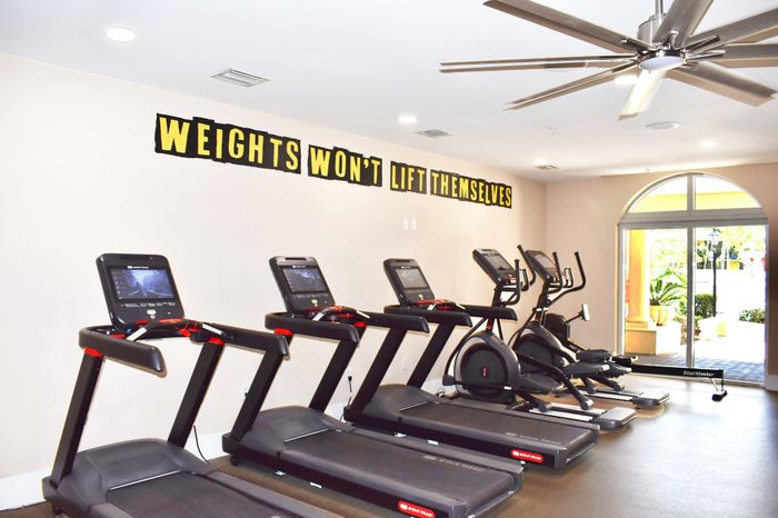 Modern fitness center equipped with treadmills and elliptical machines, featuring motivational wall decor in a bright and inviting space.