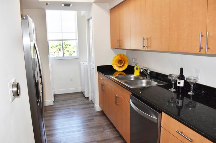 Bright and elegant kitchen with warm wooden cabinets, sleek black countertops, and a touch of nature with a vibrant sunflower centerpiece. Includes modern appliances and a large window for natural light.