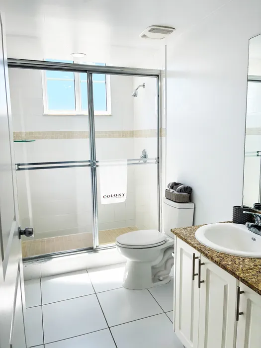 Bright, modern bathroom featuring elegant glass shower, granite countertop vanity, and sleek white tiles.
