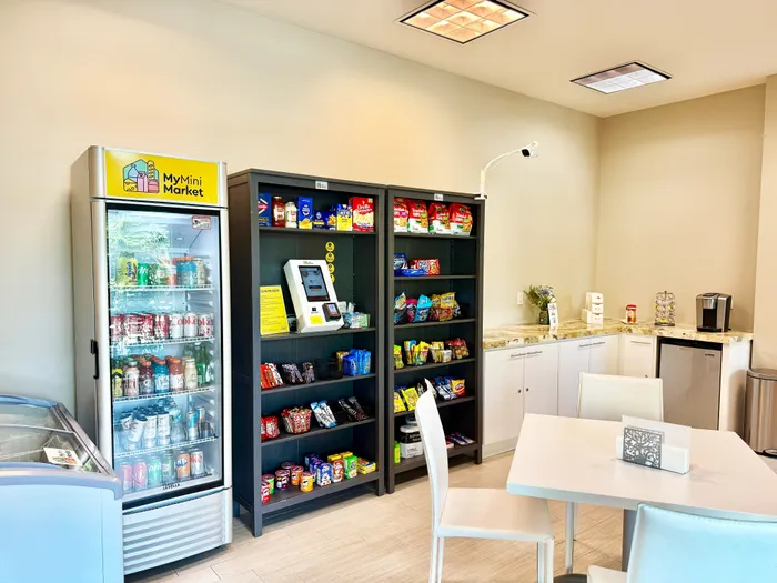 Bright and inviting mini market area featuring a stocked beverage cooler, snack shelves, and a cozy seating space.
