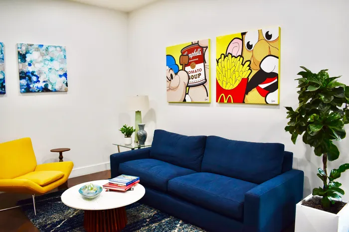 Bright and stylish living room featuring vibrant pop art, a modern navy blue sofa, and a chic yellow armchair, creating a lively and inviting atmosphere.