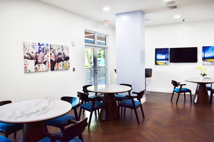Chic and inviting communal space with modern round tables, stylish seating, vibrant artwork, and natural light filtering through glass doors.