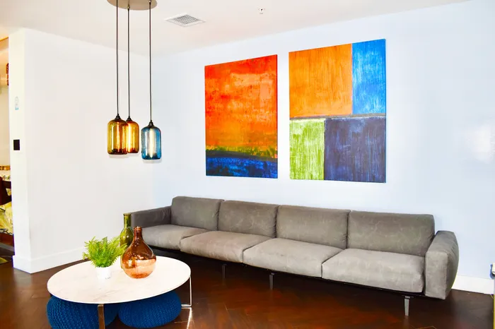 Modern living room with a chic grey sofa, vibrant abstract art, stylish pendant lights, and a sleek marble coffee table creating a cozy and elegant atmosphere.