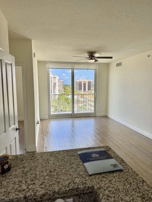 Bright living room with modern ceiling fan and large windows offering a stunning city view, complemented by sleek laminate flooring.