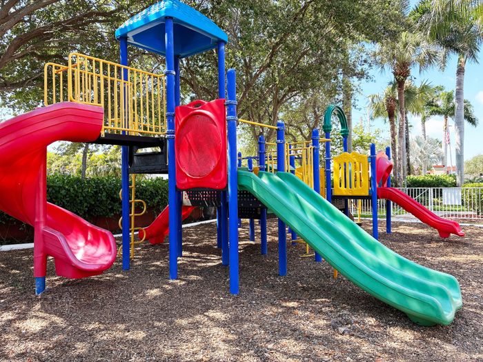 Vibrant outdoor playground with colorful slides and climbing structures, set amidst lush greenery and palm trees.