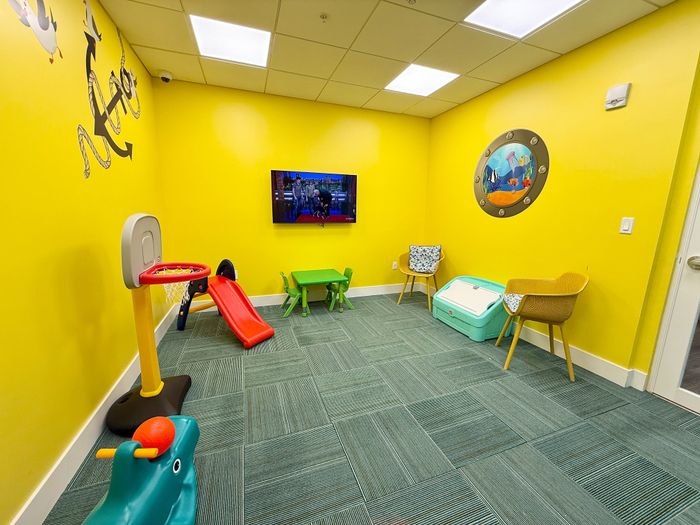 Vibrant children's playroom with cheerful yellow walls, featuring a mini basketball hoop, slide, and cozy seating for fun and relaxation.