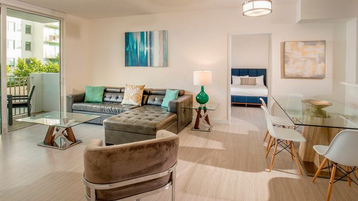 Bright and modern apartment living room with stylish leather seating, glass coffee table, chic dining area, and balcony access, offering a cozy and inviting atmosphere.