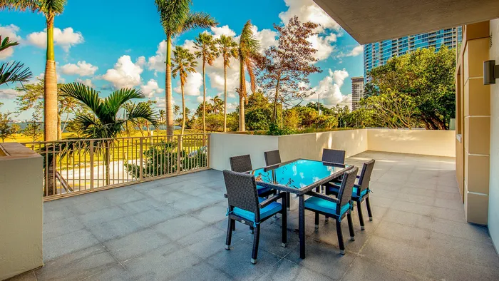 Sunny outdoor patio with modern seating and vibrant tropical palms, offering a serene view of lush greenery.