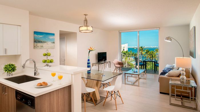 Modern apartment interior featuring an open-concept kitchen, dining, and living area with stunning ocean view, sleek furnishings, and natural light.