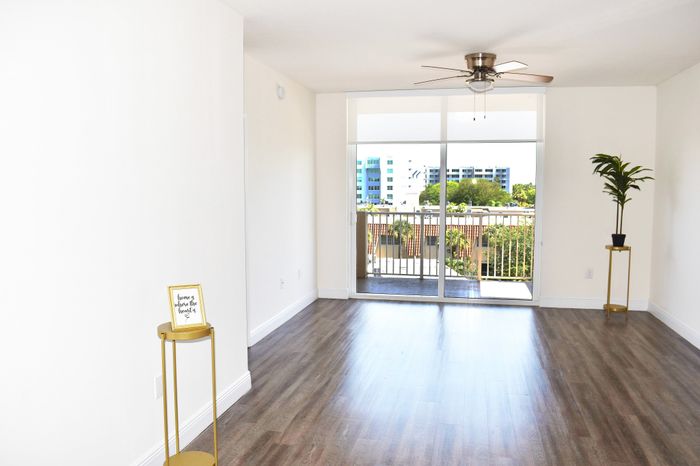Bright living room with sleek wooden floors, modern ceiling fan, and a sunlit balcony view.