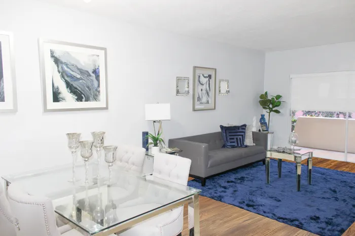Elegant living room with a modern gray sofa, chic glass dining table, and plush blue rug, accented by stylish decor and artwork.
