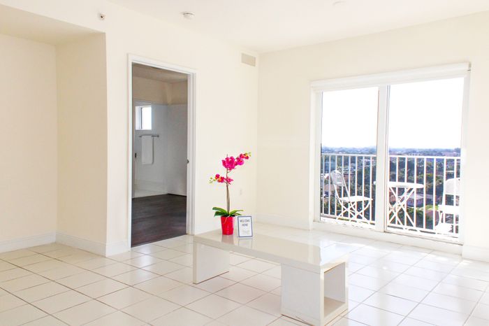 Bright and elegant living space with a minimalist coffee table, vibrant plant decor, and access to a scenic balcony view.