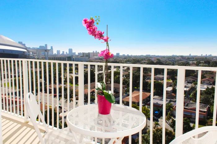 Chic balcony with panoramic city views, vibrant pink orchid centerpiece, and modern white furniture, perfect for relaxation and enjoying sunsets.